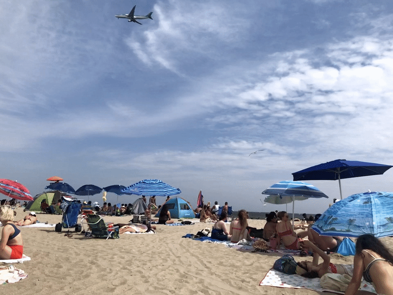 looped gif of airplane flying overhead some crowds at a beach